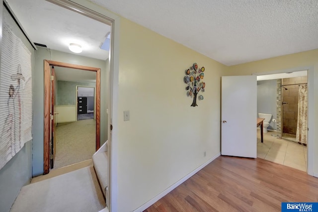 hallway featuring a textured ceiling, baseboards, and wood finished floors