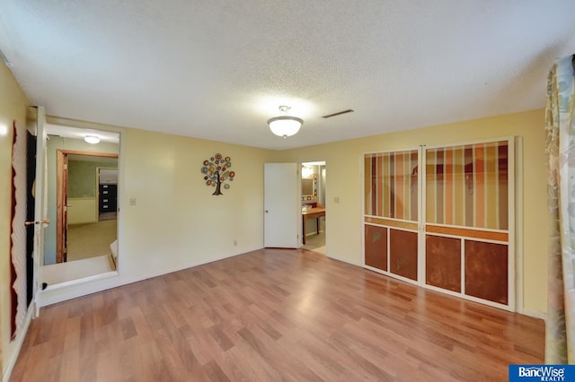 empty room with a textured ceiling, wood finished floors, and visible vents