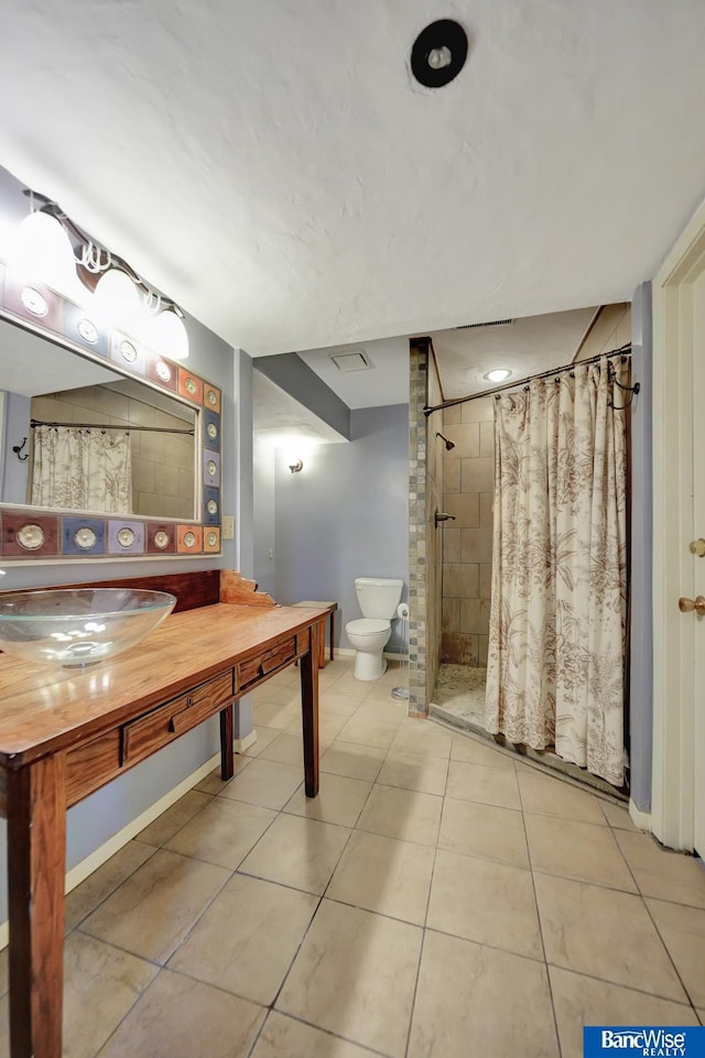 bathroom with baseboards, toilet, vanity, tile patterned floors, and tiled shower