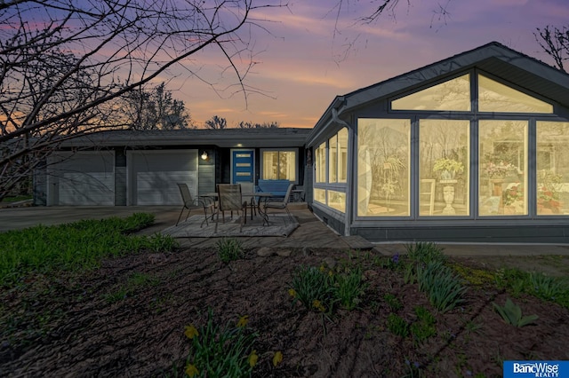 back of property with an attached garage, a patio, driveway, and a sunroom
