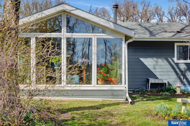 view of side of home featuring a sunroom, roof with shingles, and a yard