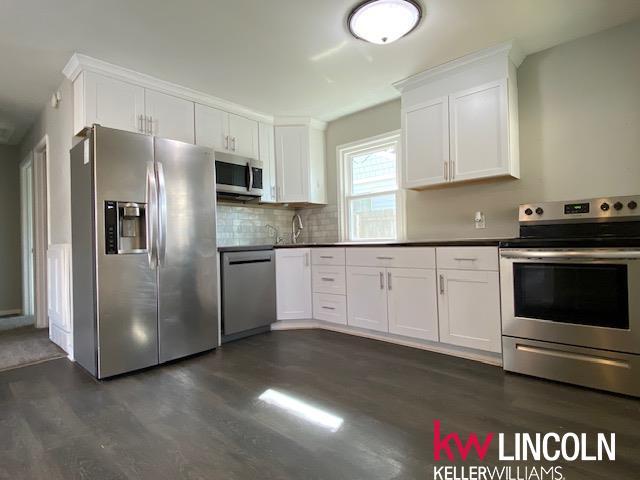 kitchen with tasteful backsplash, white cabinetry, dark wood-style flooring, dark countertops, and stainless steel appliances