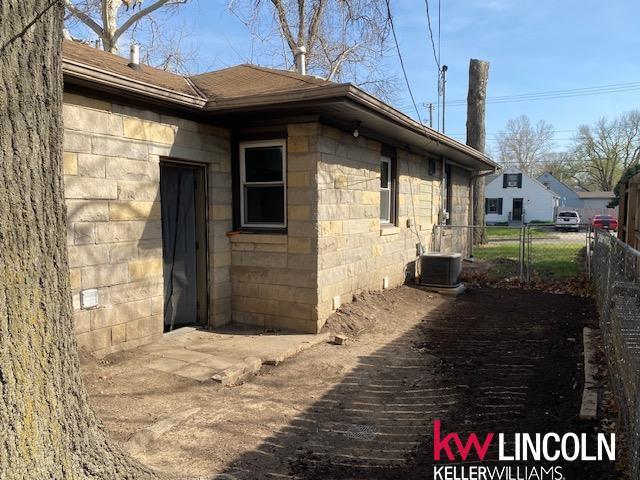 view of home's exterior with roof with shingles, central AC, and fence