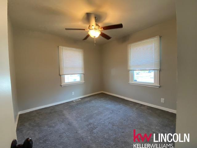 empty room with visible vents, a wealth of natural light, a ceiling fan, and baseboards