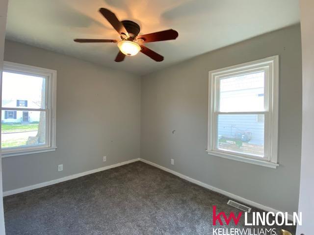 unfurnished room with dark carpet, baseboards, a ceiling fan, and visible vents