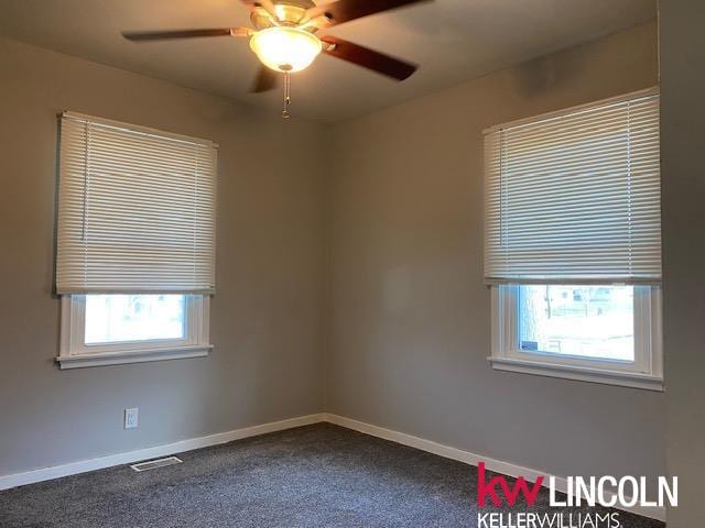 spare room with dark carpet, ceiling fan, visible vents, and plenty of natural light