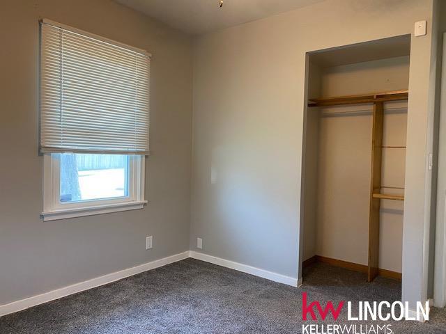 unfurnished bedroom with dark carpet, baseboards, and a closet