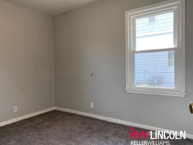 spare room featuring dark colored carpet, baseboards, and a healthy amount of sunlight