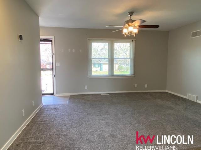 empty room featuring dark carpet, ceiling fan, and visible vents