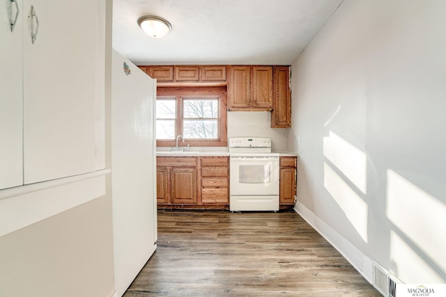 kitchen with a sink, light countertops, white appliances, brown cabinets, and wood finished floors