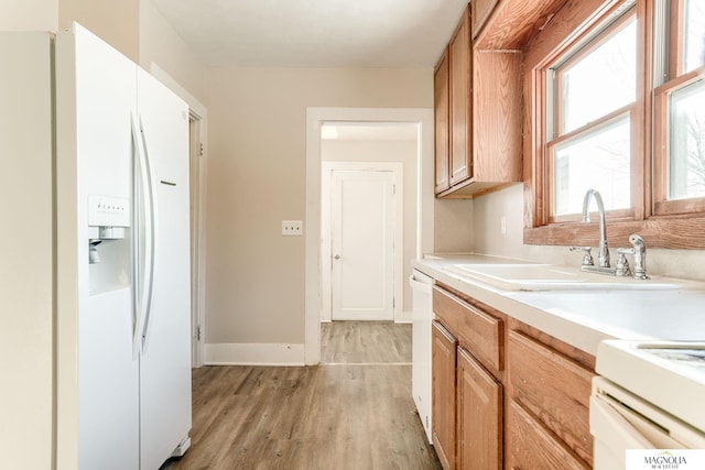 kitchen featuring baseboards, white appliances, light countertops, light wood-style floors, and a sink