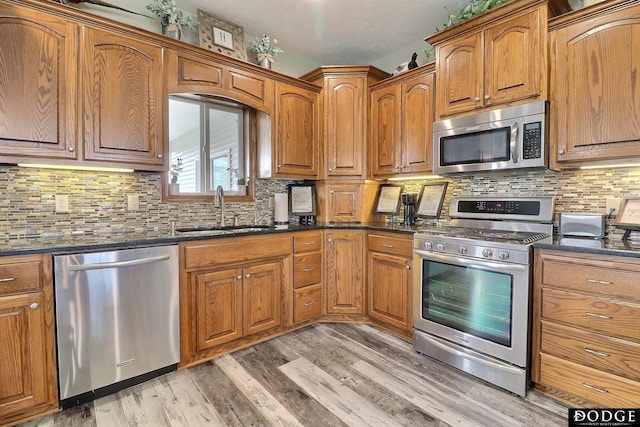kitchen featuring backsplash, light wood-style floors, brown cabinets, stainless steel appliances, and a sink