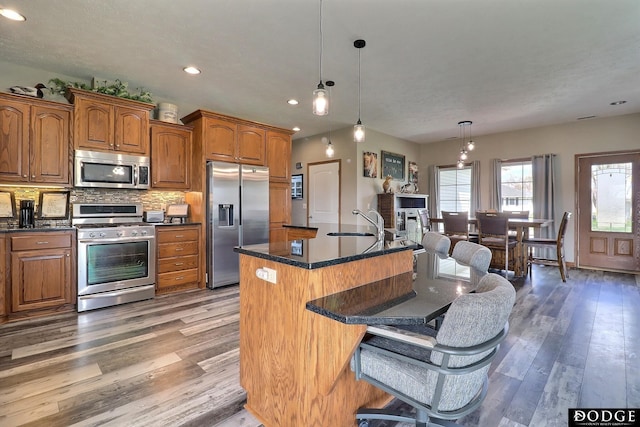 kitchen with brown cabinets, a breakfast bar area, appliances with stainless steel finishes, and wood finished floors