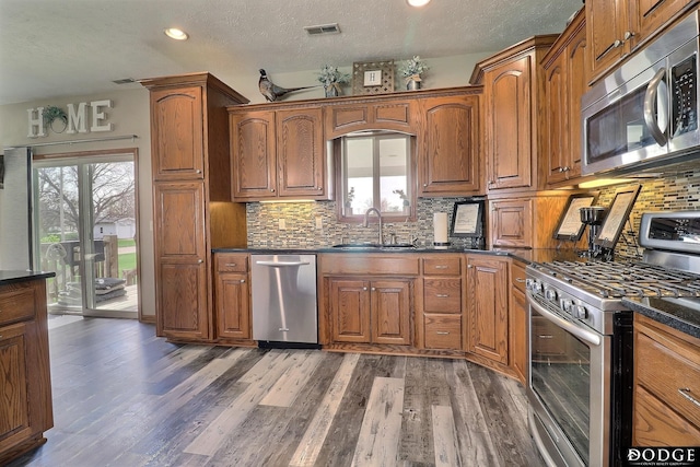 kitchen with brown cabinetry, visible vents, dark countertops, a sink, and stainless steel appliances