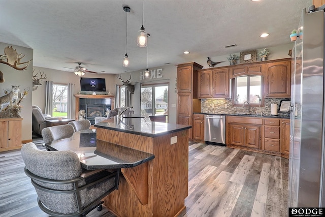 kitchen featuring a fireplace, light wood-type flooring, dark countertops, stainless steel appliances, and open floor plan