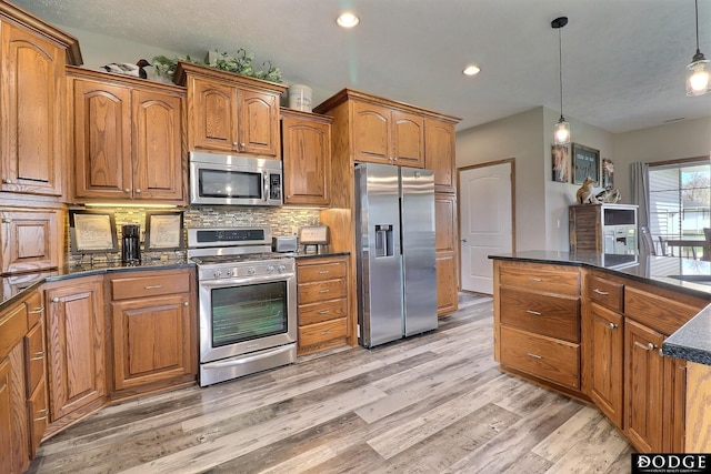 kitchen with decorative light fixtures, light wood-type flooring, brown cabinets, and stainless steel appliances