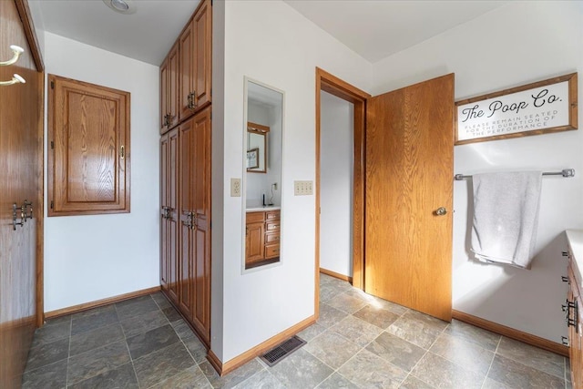 hallway featuring visible vents, baseboards, and stone finish flooring