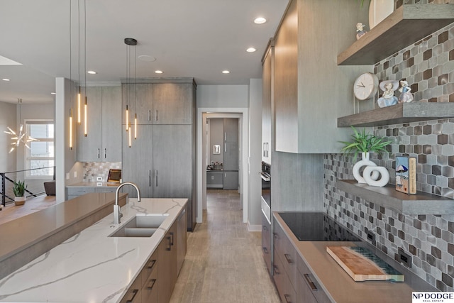 kitchen with modern cabinets, tasteful backsplash, recessed lighting, light stone counters, and a sink