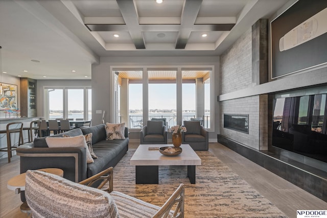 living room with a brick fireplace, a water view, beamed ceiling, wood finished floors, and coffered ceiling
