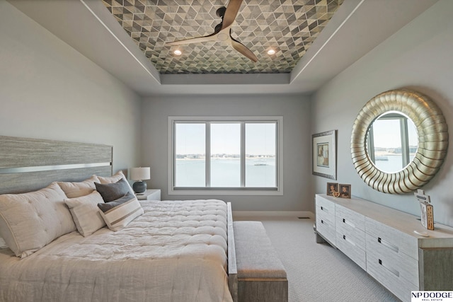 bedroom with a raised ceiling, baseboards, carpet, and a water view
