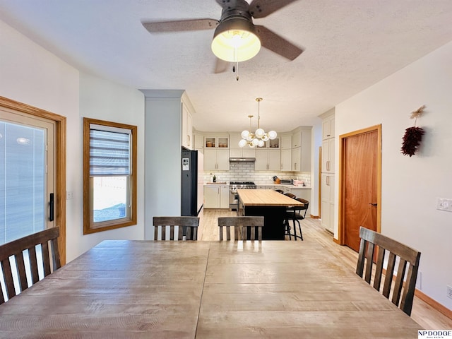 dining room featuring light wood-style floors, ceiling fan with notable chandelier, and a textured ceiling