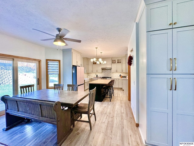 dining space with ceiling fan with notable chandelier, light wood-style flooring, baseboards, and a textured ceiling