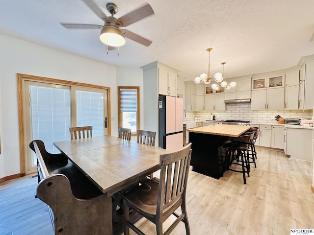 dining space with light wood-style flooring, ceiling fan with notable chandelier, and baseboards