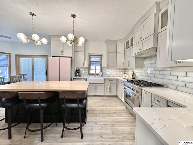 kitchen with a notable chandelier, freestanding refrigerator, stainless steel stove, light wood finished floors, and light stone counters