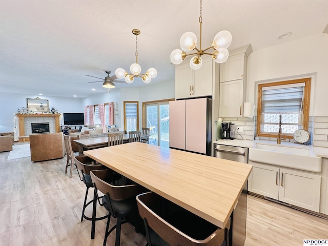 interior space with light wood finished floors, plenty of natural light, a tile fireplace, and ceiling fan with notable chandelier