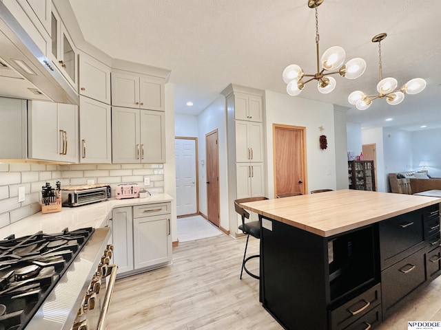 kitchen with a notable chandelier, wooden counters, dark cabinetry, light wood-style floors, and under cabinet range hood