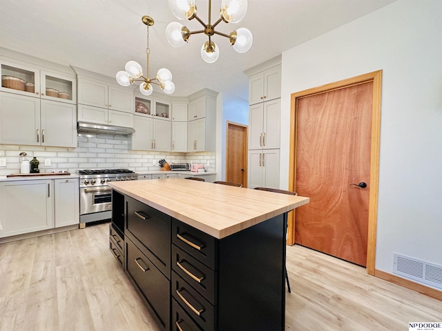 kitchen with an inviting chandelier, dark cabinets, butcher block counters, visible vents, and stainless steel range
