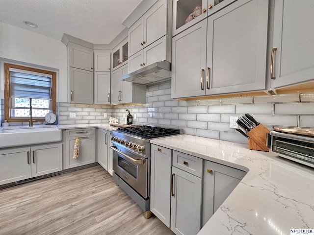 kitchen with high end stainless steel range oven, tasteful backsplash, gray cabinetry, under cabinet range hood, and light wood-style floors