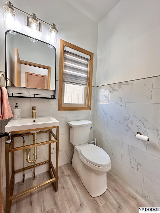 half bath featuring toilet, wood finished floors, a sink, and tile walls