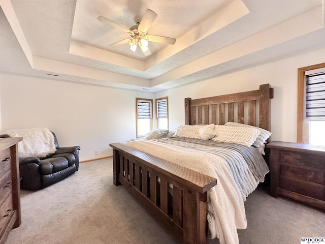 carpeted bedroom featuring a raised ceiling, baseboards, and multiple windows