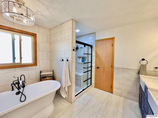 bathroom featuring a shower stall, a textured ceiling, vanity, tile walls, and a freestanding bath