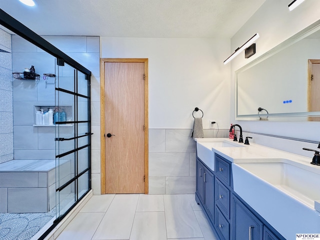 bathroom with a sink, tile walls, double vanity, tiled shower, and tile patterned flooring