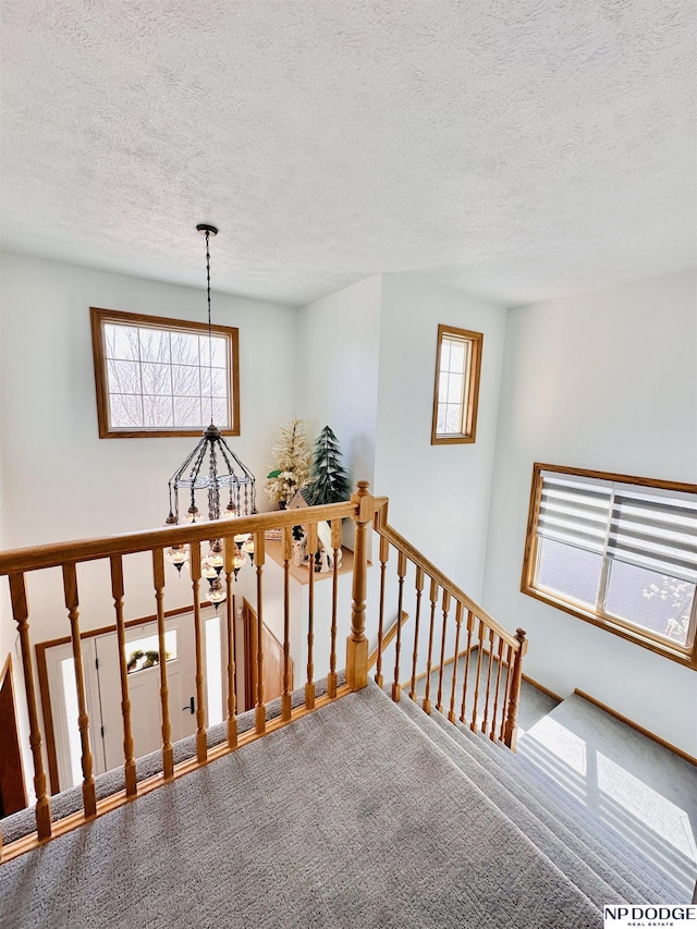 staircase featuring carpet, a notable chandelier, and a textured ceiling