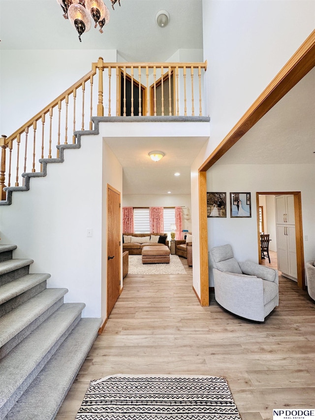 foyer with light wood-style flooring, a towering ceiling, and stairway