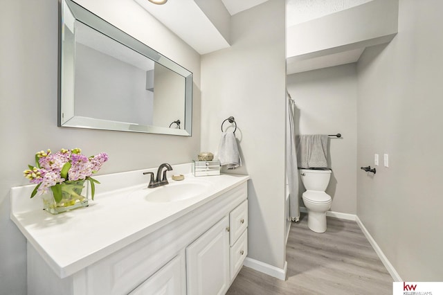 bathroom featuring vanity, toilet, a shower with shower curtain, baseboards, and wood finished floors