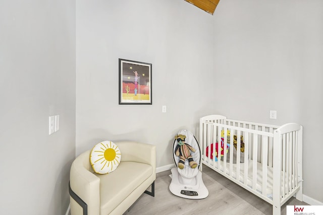 bedroom with a crib, baseboards, vaulted ceiling, and wood finished floors