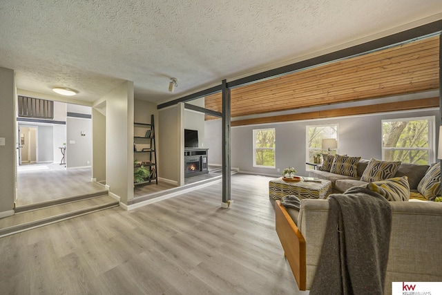living room featuring baseboards, a textured ceiling, a warm lit fireplace, and wood finished floors