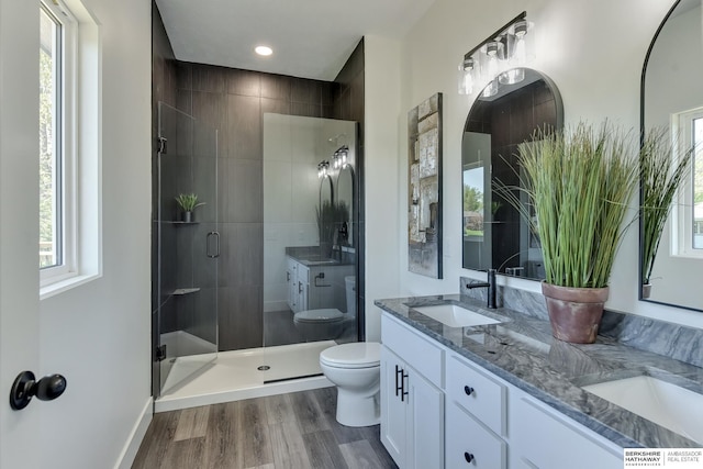full bath featuring a sink, double vanity, toilet, a shower stall, and wood finished floors
