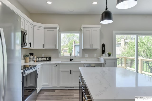 kitchen featuring appliances with stainless steel finishes, light stone countertops, a sink, recessed lighting, and light wood-style flooring