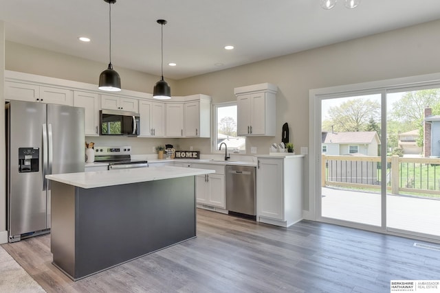 kitchen with appliances with stainless steel finishes, light wood-style floors, light countertops, a kitchen island, and pendant lighting