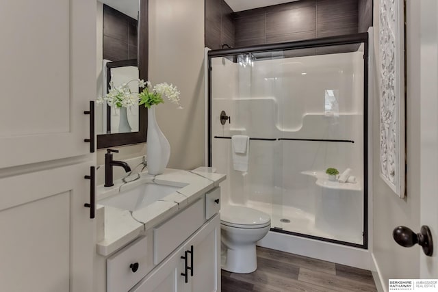 bathroom featuring wood finished floors, a stall shower, toilet, and vanity