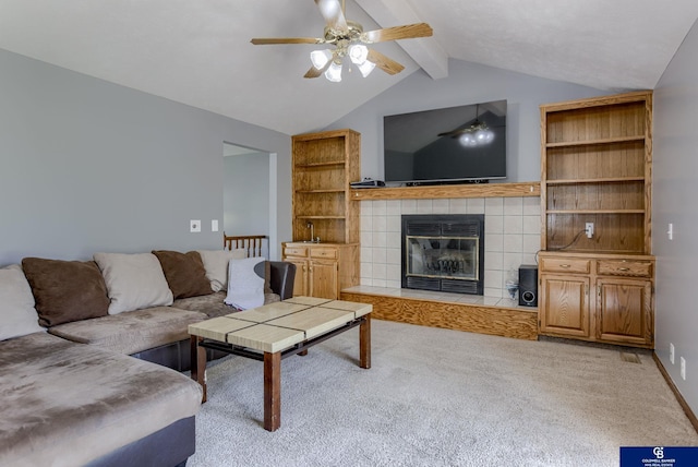 living room featuring a ceiling fan, a tiled fireplace, vaulted ceiling with beams, and carpet