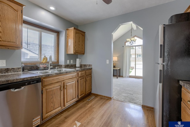 kitchen with ceiling fan with notable chandelier, dark countertops, a sink, light wood finished floors, and appliances with stainless steel finishes
