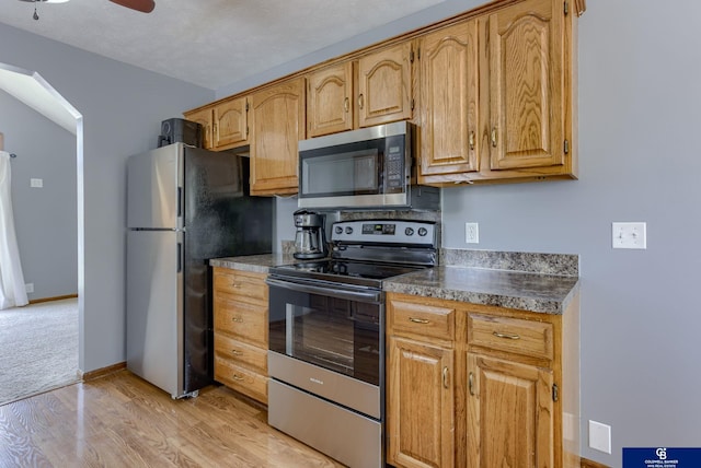 kitchen featuring baseboards, arched walkways, a ceiling fan, light wood finished floors, and stainless steel appliances