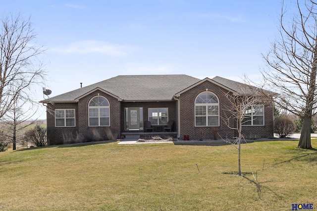 ranch-style house featuring brick siding, a front yard, and roof with shingles