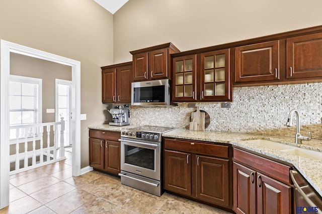 kitchen with high vaulted ceiling, glass insert cabinets, tasteful backsplash, appliances with stainless steel finishes, and a sink